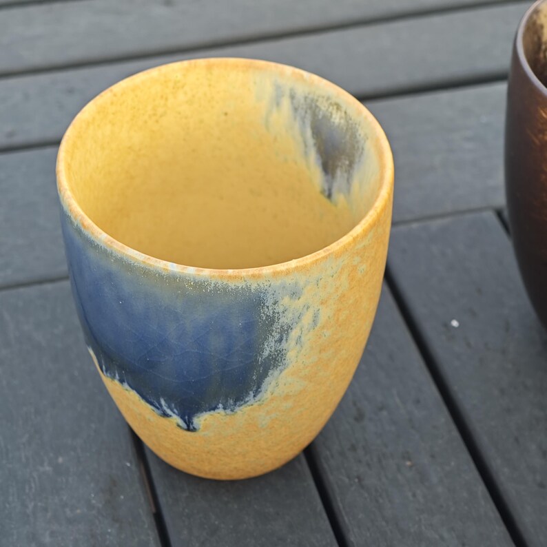 Puede incluir: Una taza de cer&aacute;mica hecha a mano con un dise&ntilde;o &uacute;nico. La taza presenta un exterior amarillo con una banda azul cerca de la base. El interior tambi&eacute;n es amarillo. La taza es de un tama&ntilde;o perfecto para caf&eacute; o t&eacute;.