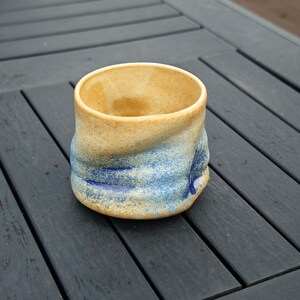 Peut inclure: Un mug en c&eacute;ramique fait &agrave; la main avec un design textur&eacute; unique. L'int&eacute;rieur et le bord du mug sont de couleur beige clair, passant &agrave; un motif tachet&eacute; bleu et blanc &agrave; l'ext&eacute;rieur. Le mug mesure environ 7.6 cm de haut.