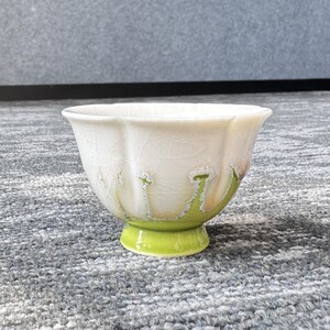 Pode incluir: Uma tigela de cer&acirc;mica branca com borda ondulada e esmalte craquelado. A tigela tem uma base verde e detalhes verdes. A tigela &eacute; provavelmente usada para servir ou expor.