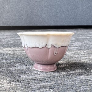 Pode incluir: Uma tigela de cer&acirc;mica com base de pedestal. A tigela tem um exterior rosa claro com uma borda branca texturizada. A forma da tigela lembra uma flor. A tigela est&aacute; em uma superf&iacute;cie cinza.