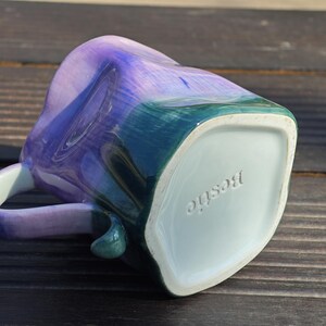 May include: A ceramic mug with a heart-shaped design, featuring a blend of blue, purple, and green hues. The word "Bestie" is embossed on the bottom of the mug. The handle is a matching color.