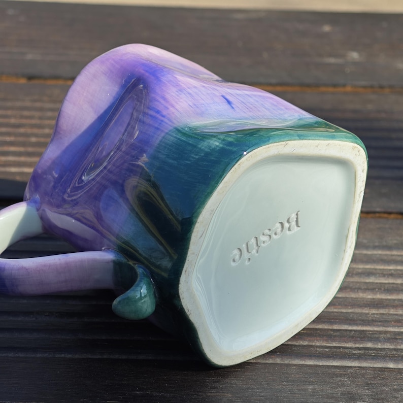 May include: A ceramic mug with a heart-shaped design, featuring a blend of blue, purple, and green hues. The word "Bestie" is embossed on the bottom of the mug. The handle is a matching color.