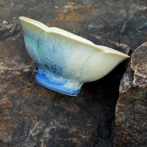 May include: A ceramic bowl with a unique, organic shape. The bowl features a gradient of colors, transitioning from a creamy off-white to shades of blue and green. The base is a vibrant blue.