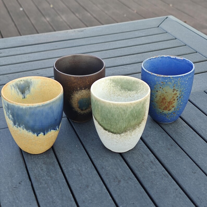 Puede incluir: Cuatro vasos de cer&aacute;mica hechos a mano con gradientes de color &uacute;nicos. Los vasos presentan tonos de azul, amarillo, marr&oacute;n y verde. Cada vaso tiene un dise&ntilde;o y una textura diferentes, perfectos para bebidas.
