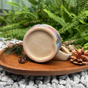 Peut inclure: Une tasse en céramique avec une anse beige mouchetée et un extérieur émaillé multicolore. Le fond de la tasse est non émaillé, de couleur beige clair, et porte l'inscription "Bestie Ever" en lettres sombres et simples.