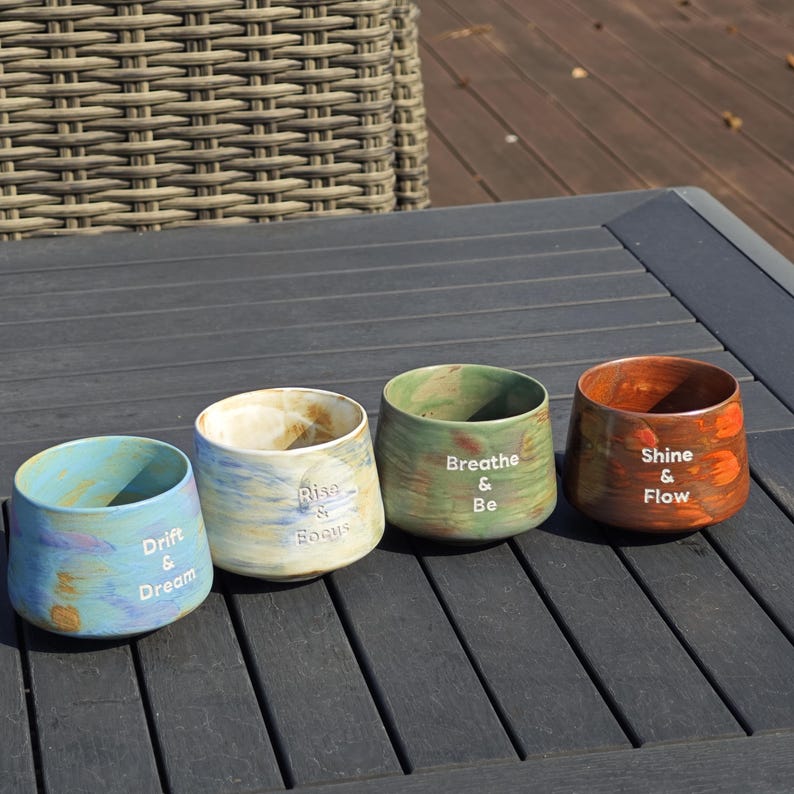 May include: Four small, ceramic pots with a marbled finish in shades of blue, green, and orange. Each pot has a different inspirational phrase in white: "Drift & Dream", "Rise & Focus", "Breathe & Be", and "Shine & Flow".