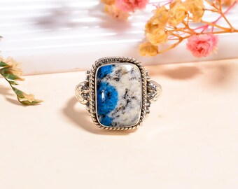 May include: A silver ring with a rectangular k2 stone. The stone features a mix of blue, white, and black patterns. The ring has a rope-like border and decorative elements on the sides, showcasing a unique and artistic design.