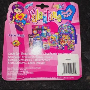 May include: A pink Lisa Frank Valentine's Day package with a cartoon girl holding a heart. The package includes a backpack, stationery, and stickers. Text includes "9 Fun Rings" and "Lisa Frank".
