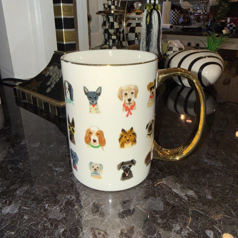 Op de afbeelding: Witte keramische mok met een gouden handvat en rand, versierd met kleurrijke illustraties van verschillende hondenrassen. De mok heeft een standaardformaat voor koffie of thee.