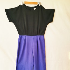 Könnte beinhalten: Ein schwarzer und lilafarbener Jumpsuit mit kurzen Ärmeln. Die obere Hälfte des Jumpsuits ist schwarz und die untere Hälfte ist lila.