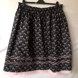 May include: A black skirt with a pink floral print and a pink lace trim. The skirt has an elastic waistband and a gathered design.