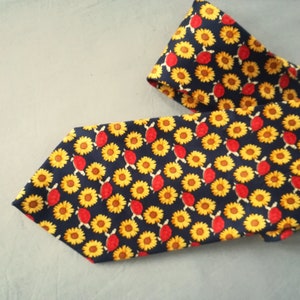 Może przedstawiać: Granatowy krawat z powtarzającym się wzorem żółtych słoneczników i czerwonych żółwi.