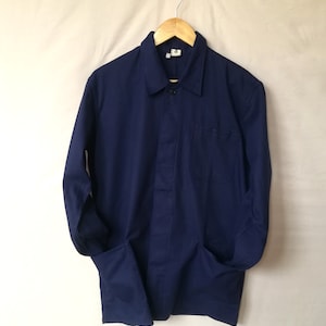 Puede incluir: Una chaqueta de trabajo azul oscuro con mangas largas, cierre de botones y dos bolsillos.