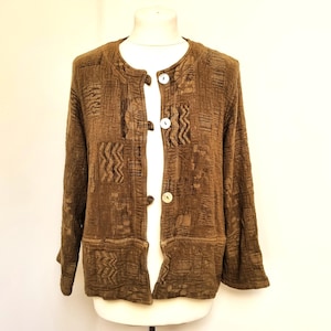 Op de afbeelding: Bruine jas met een textuurpatroon, lange mouwen en drie witte knopen. De jas heeft een ronde halslijn en wordt op een mannequin gepresenteerd. Het ontwerp omvat geometrische vormen.