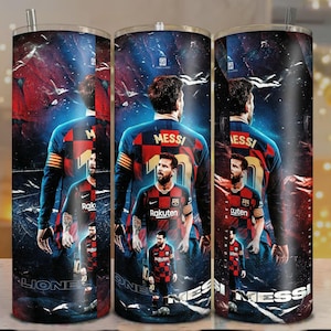 Puede incluir: Un vaso de acero inoxidable con un diseño de un jugador de fútbol con una camiseta roja y azul. El vaso tiene un fondo negro con el nombre del jugador y la palabra "MESS" impresa. El vaso tiene una pajita plateada.