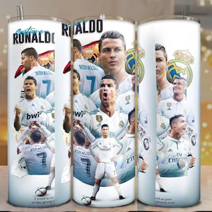 Puede incluir: Un vaso blanco con pajita plateada, decorado con múltiples imágenes de Cristiano Ronaldo. El diseño incluye texto como "Ronaldo" y "Real Madrid". El vaso muestra un collage de Ronaldo en varias poses de fútbol.