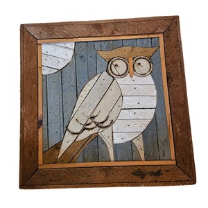 May include: A square wooden wall art piece featuring a mosaic of an owl against a blue-grey vertical plank background with a white moon. The owl is constructed from light-colored wood slats. The name degroot is written in the bottom right corner.