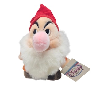 May include: A plush Grumpy doll from Disney's Snow White and the Seven Dwarfs. The doll features a red hat, a large pink nose, and a white beard. The Disney Store tag is attached.
