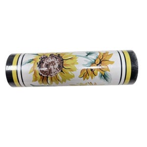 May include: A cylindrical decorative item featuring a sunflower design. The item has a white background with yellow sunflowers and green leaves. The ends are black with yellow and white stripes. The item is approximately 8 inches long.