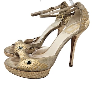 May include: Beige suede platform sandals with a high heel and ankle strap. The sandals feature embroidered flowers and bee accents.