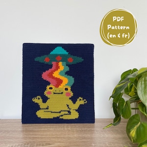 May include: A navy blue cross-stitch art piece featuring a yellow frog in a meditative pose, with a colorful beam emanating from a teal UFO above. The text "PDF Pattern (en & fr)" is in a gold circle.