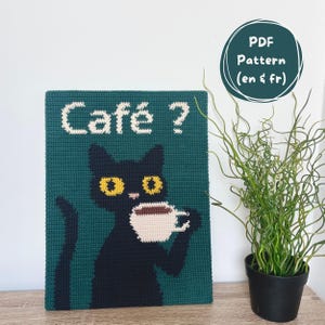 Peut inclure: Une tenture murale au crochet verte représentant un chat noir buvant du café. Le chat a des yeux jaunes et une tasse blanche. Les mots "Café ?" sont en blanc au-dessus du chat. Un patron PDF est également disponible.