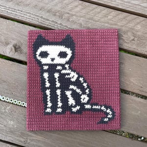 Peut inclure: Carr&eacute; crochet&eacute; avec un motif de chat squelette noir et blanc sur fond bordeaux. Le chat est assis, avec les d&eacute;tails de son squelette visibles. Cet article fait main est adapt&eacute; pour les d&eacute;corations d'Halloween.