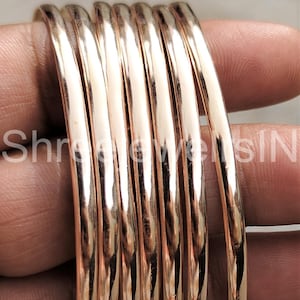 May include: A set of gold-colored bangles, stacked together. The bangles are smooth and shiny, reflecting light. The text "Shree Jewels SIN" is visible on the left side of the image. The bangles are a warm, metallic color.