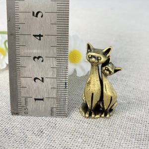Op de afbeelding: Een kleine kattenfiguur van messing in antieke stijl. De figuur toont twee katten, waarvan &eacute;&eacute;n de ander omarmt. De katten zijn ongeveer 3,8 cm hoog. De figuur heeft een vintage uitstraling.