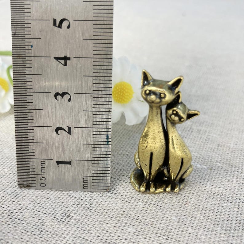 Op de afbeelding: Een kleine kattenfiguur van messing in antieke stijl. De figuur toont twee katten, waarvan &eacute;&eacute;n de ander omarmt. De katten zijn ongeveer 3,8 cm hoog. De figuur heeft een vintage uitstraling.