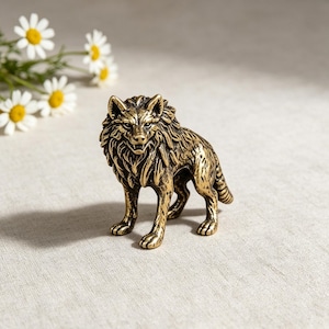 Può includere: Una piccola statuetta di lupo in metallo color ottone in una posa vigile. La scultura presenta un pelo dettagliato e strutturato, orecchie a punta e una bocca leggermente aperta che mostra i denti. La finitura ha una lucentezza levigata.
