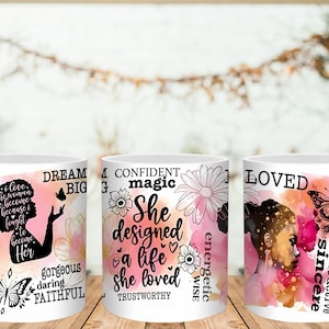 May include: Three white ceramic mugs with inspirational quotes and floral and butterfly designs. One mug features a silhouette of a woman with the words "Dream Big." Another mug has the words "She designed a life she loved." The third mug has the word "Loved."