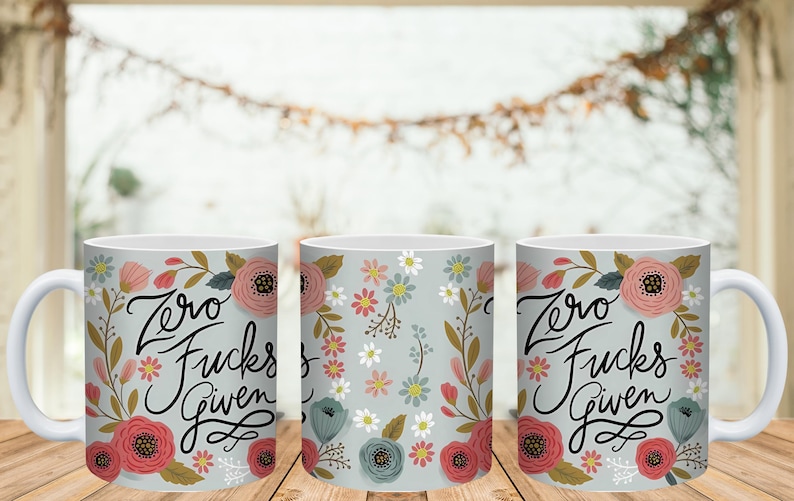 May include: Three white ceramic mugs with floral designs and the phrase "Zero Fucks Given" in black script. The mugs feature pink, red, and blue flowers on a light gray background.