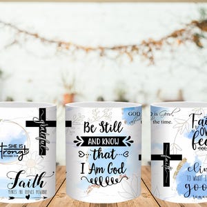 May include: White ceramic mugs with inspirational quotes and floral designs. Each mug features a black cross and text like "Strong," "Be Still," and "Faith Over Fear." The mugs have a light blue and gold color scheme.