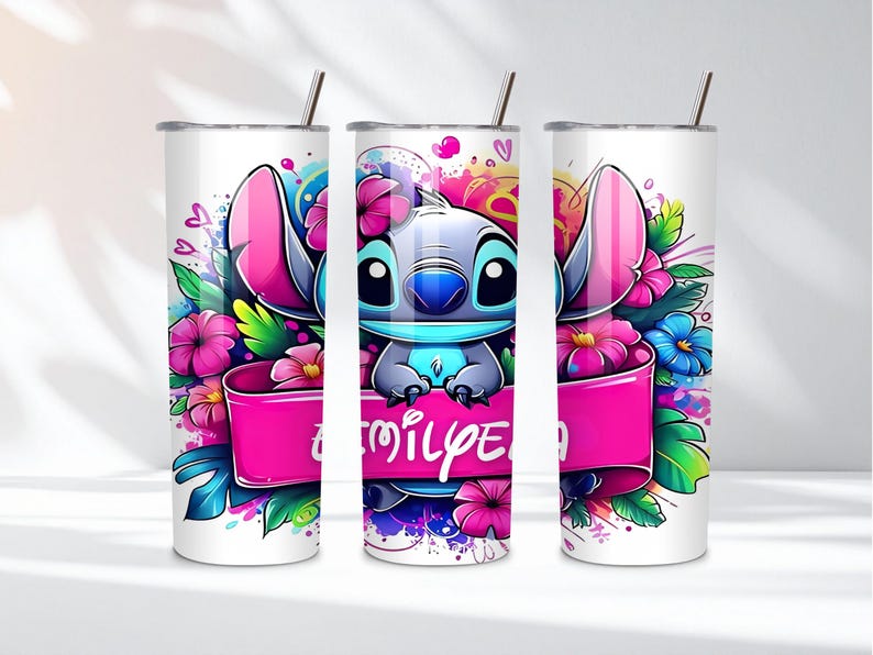K&ouml;nnte beinhalten: Ein wei&szlig;er Becher mit einer farbenfrohen Illustration der Figur Stitch, umgeben von rosa und blauen Blumen. Ein rosa Banner mit dem Wort "family" ist zu sehen. Der Becher hat einen silbernen Strohhalm.