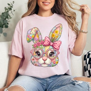 Könnte beinhalten: Hellrosa T-Shirt mit einem bunten Hasengesicht-Design. Der Hase hat herzförmige Brille, eine rosa Schleife und florale Akzente. Das Design besteht aus Patchwork mit Blumen und anderen Mustern.