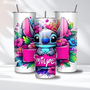 K&ouml;nnte beinhalten: Drei wei&szlig;e Edelstahlbecher mit einem Cartoon-Charakter-Design. Das Design zeigt eine blau-graue, au&szlig;erirdische Kreatur mit gro&szlig;en rosa Ohren, umgeben von bunten Blumen und einem rosa Banner mit Text.