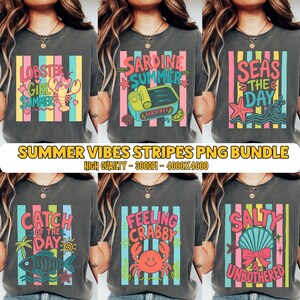 May include: A collection of six charcoal gray t-shirts featuring colorful graphic prints with vertical stripes and summer-themed text including Lobster Girl Summer, Sardine Summer, Seas The Day, Catch Of The Day, Feeling Crabby, and Salty Unbothered.