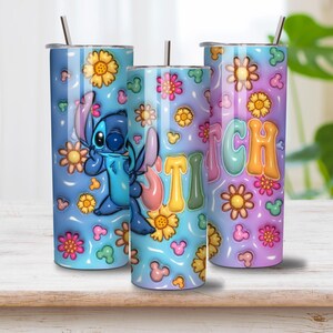 May include: Three cylindrical tumblers with metal straws featuring a blue and purple gradient background. The design includes a blue character, yellow and pink flowers, small mouse-ear shapes, and the word STITCH in large, colorful bubble letters.
