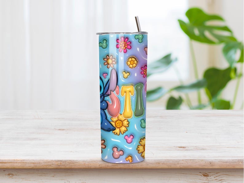 May include: A cylindrical stainless steel tumbler featuring a light blue background with a repeating pattern of colorful flowers and small mouse-ear silhouettes. The blue character Stitch is visible on the side, along with the letters STI in a puffy font.