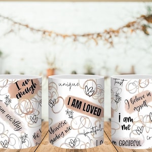 May include: White ceramic mugs with inspirational phrases like "I am enough" and "I am loved" in black script. The mugs feature abstract line art, hearts, and floral accents in a neutral color palette. The mugs are on a wooden surface.