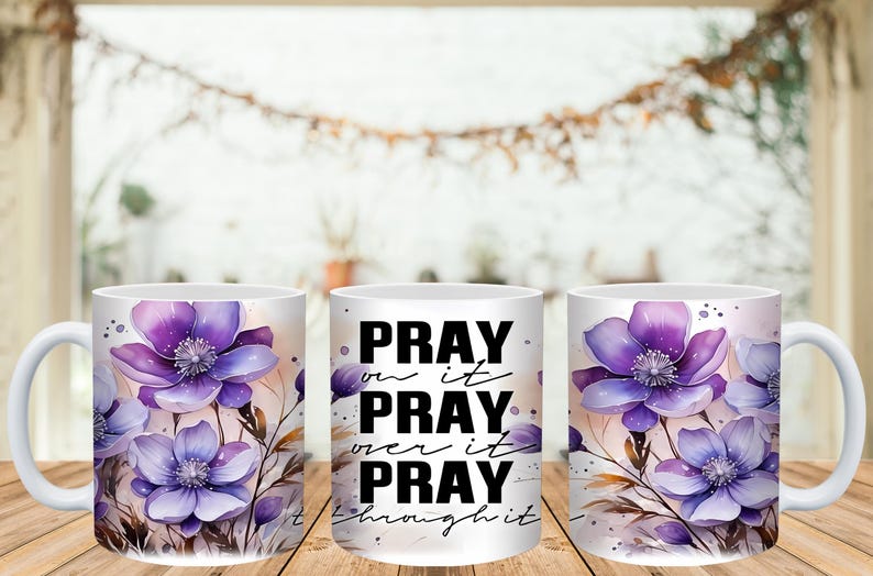 May include: White ceramic coffee mug featuring watercolor purple flowers and the text "PRAY on it, PRAY over it, PRAY through it." The floral design includes purple and lavender blooms with green stems and leaves. The mug has a white handle.