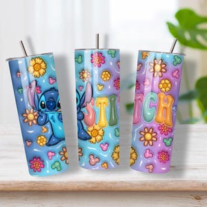 May include: Three cylindrical tumblers with metal straws featuring a blue and purple gradient background. The design includes a blue alien character, colorful flowers, small mouse-ear silhouettes, and the word STITCH in large, puffy, multi-colored letters.