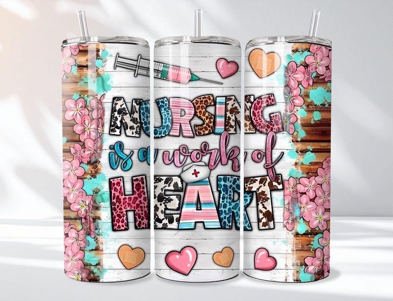 May include: A set of three stainless steel tumblers with a floral and wood grain design. The tumblers feature the text "NURSING is a work of HEART" with a syringe and heart graphics. Pink flowers and hearts decorate the sides.