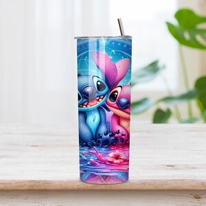 Puede incluir: Un vaso cil&iacute;ndrico de acero inoxidable con un estampado gr&aacute;fico vibrante de dos personajes alien&iacute;genas azules y rosas sentados juntos. El dise&ntilde;o incluye un fondo azul estrellado, una superficie de agua reflectante con salpicaduras y una pajita.