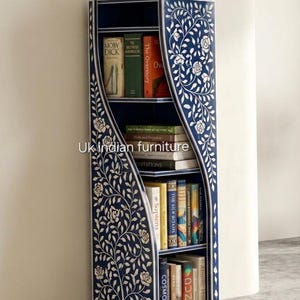 May include: A tall, narrow, dark blue bookshelf featuring intricate white floral bone inlay patterns on its curved side panels. The unit has four open shelves filled with various books and is topped with a small, light-colored decorative vase.