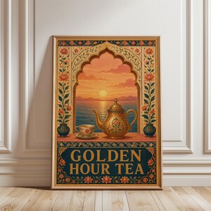 Op de afbeelding: Een ingelijste verticale wandkunstprint met een gouden theepot en theekopje op een richel voor een boogvenster met uitzicht op een zonsondergang boven de zee. De rand toont bloemmotieven en de tekst onderaan luidt GOLDEN HOUR TEA.