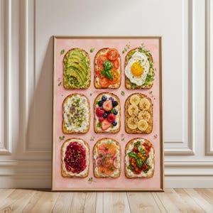 May include: A rectangular wall art print on a pink background featuring a grid of nine slices of toast topped with various ingredients including avocado, tomato, egg, berries, banana, jam, smoked salmon, and herbs, all arranged in three rows.