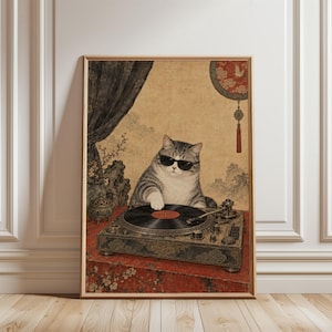 May include: A framed wall art print featuring a grey tabby cat wearing black sunglasses, positioned behind a vintage turntable. The cat has one paw on a black vinyl record. The background displays a traditional East Asian aesthetic with a red floral table cover, a hanging circular ornament with a tassel, and dark curtains.