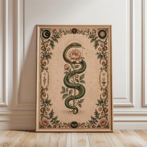 Puede incluir: Una impresión rectangular enmarcada sobre un fondo beige que presenta una serpiente verde central enroscada alrededor de una peonía rosa en flor. La obra está rodeada por un borde floral detallado con rosas, una luna creciente, un sol y pequeños símbolos.